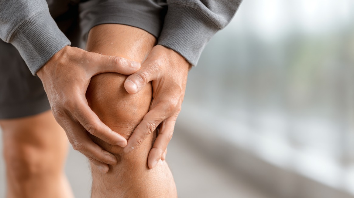 Close-up of a person holding their knee in discomfort, suggesting joint pain or strain.