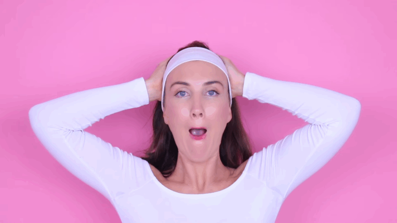 Woman performing jaw and neck firmer face exercises with hands behind her head and mouth open to engage lower face muscles