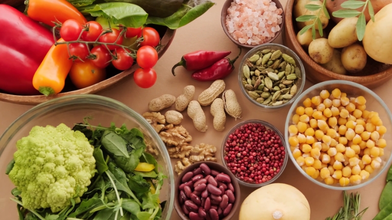 Colorful mix of fresh vegetables, nuts, legumes, and herbs arranged on a kitchen counter