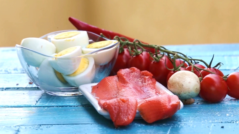 Boiled eggs, raw salmon, and fresh vegetables on a blue table showing common foods in Keto, Paleo, and DASH diets