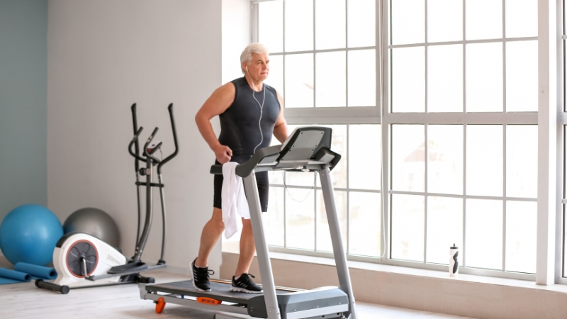 An older man walks on a treadmill during a workout focused on strength and healthy aging
