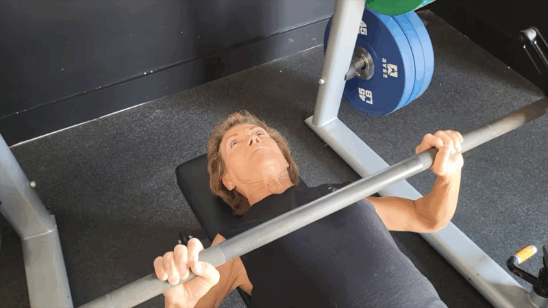 Marlene Flowers lifts a barbell during a focused bench press session at the gym in her 70s