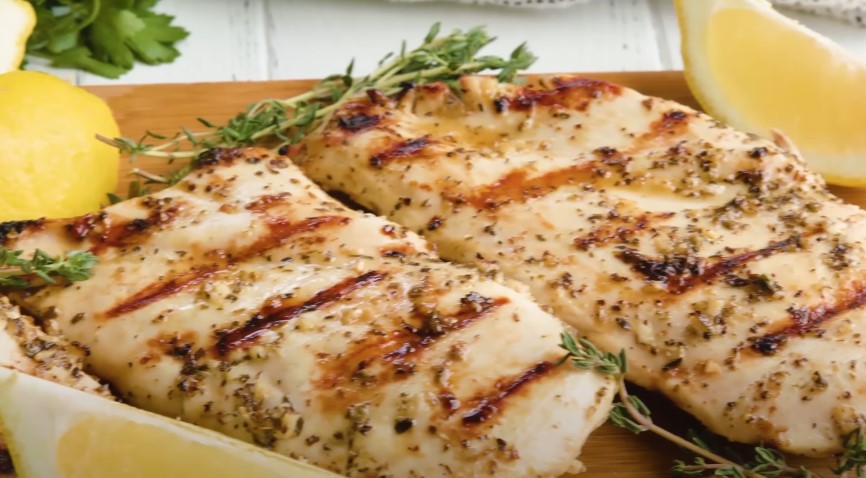 Two grilled chicken breasts, seasoned with herbs and spices, glistening with a light glaze