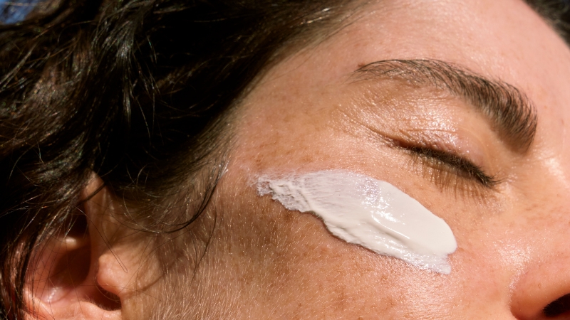 A close-up of a person applying sunscreen to their cheek as part of a pre-workout skincare routine