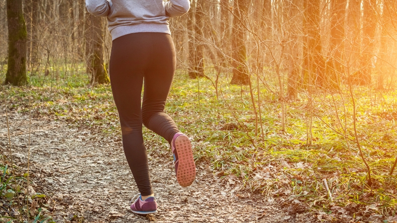Woman running alone on a forest trail at sunset, showing running alone in nature
