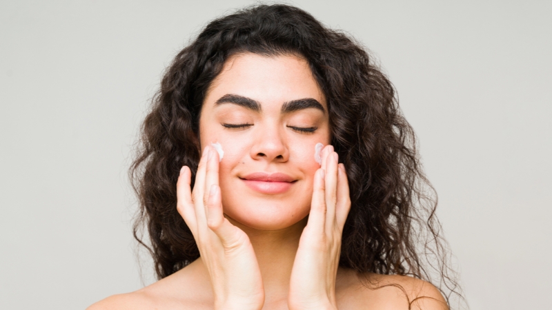 A woman applies sunscreen to her face as part of her pre-workout skincare routine