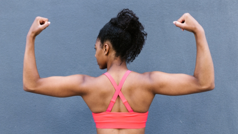 Woman flexing her arms in a workout top, showing confidence built through self-motivated fitness choices