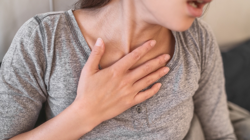 A woman holds her chest while struggling to breathe, showing signs of shortness of breath