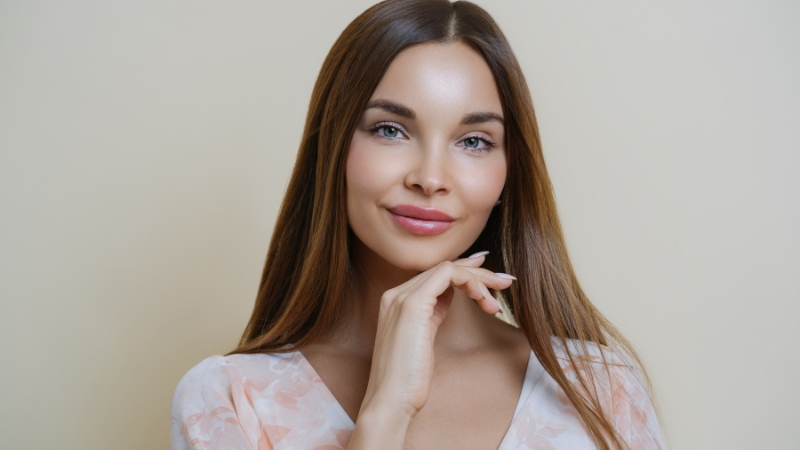 Woman holding a soft smile with her hand near her chin, demonstrating the smiler face exercise for cheek and mouth toning