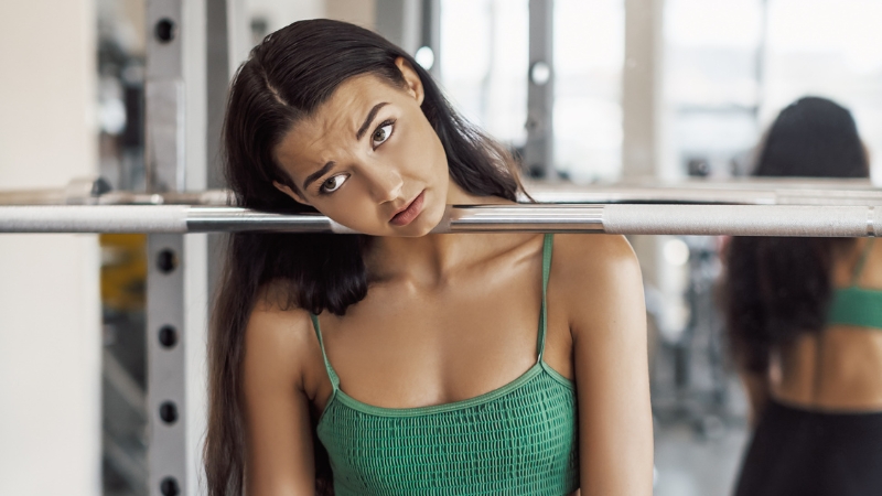 Woman at the gym looking tired and unmotivated, showing why people start skipping workouts