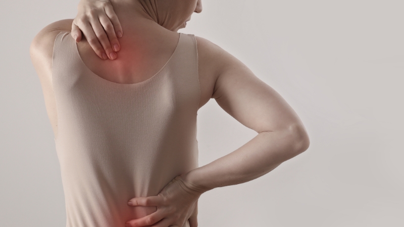 Woman holding her neck and lower back, showing signs of discomfort from poor posture