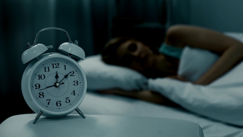 A woman rests in bed as a clock shows early morning hours, highlighting the role of deep sleep in overnight muscle recovery