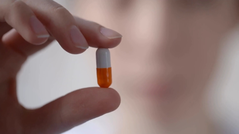 A person holds a capsule between two fingers, highlighting medication as a treatment option for neck pain