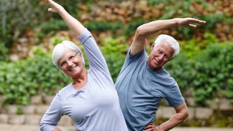 Two seniors stretch outdoors, showing how regular movement supports strength and well-being after 70