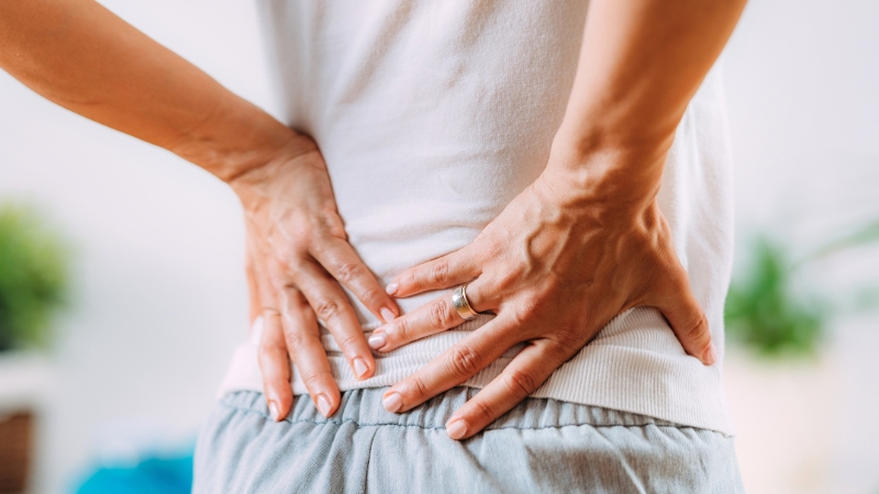 A person holds their lower back with both hands to ease discomfort from sciatic pain