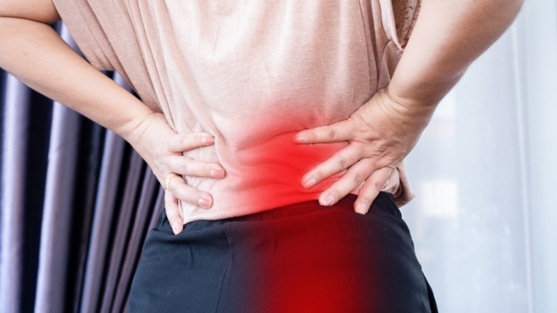 A person presses their lower back with both hands, showing discomfort from sciatic pain highlighted in red