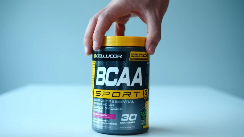 A hand reaches for a container of BCAA Sport powder with 30 servings labeled for muscle support