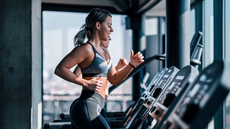 Women running on treadmills wearing fitted sports bras and high-waisted leggings designed for cardio at the gym