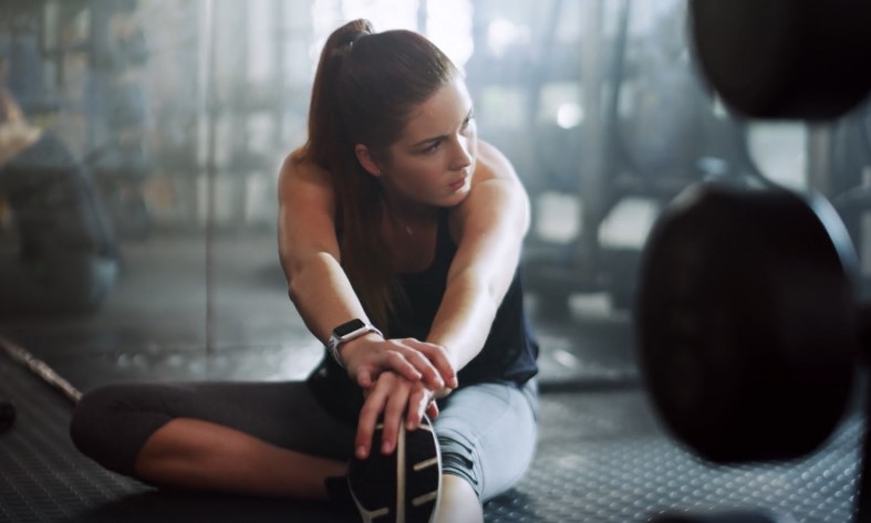 A woman stretches her legs in a gym
