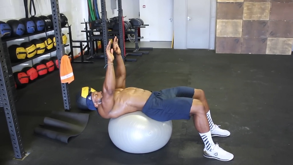 Man doing an ab curl on a stability ball with dumbbells for resistance