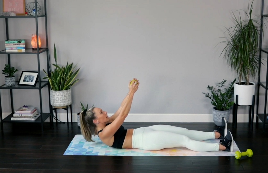 Woman doing full-body ab curl using a small dumbbell on a mat in home workout setup