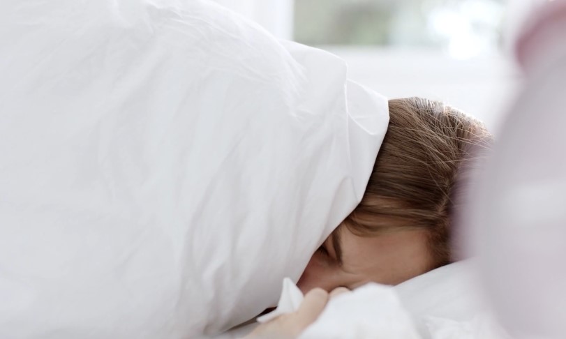 Woman laying sick in her bed, covered by white blanket