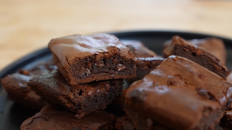 A close-up of several thick, fudgy high-protein brownies stacked on a black plate