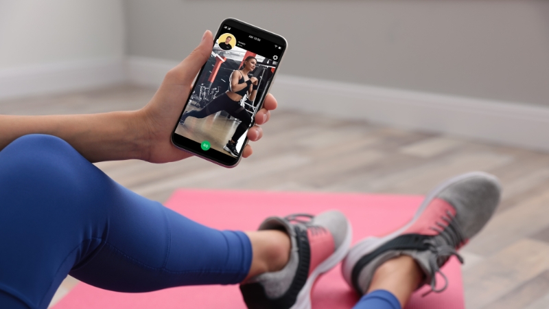 A person watches a fitness instructorโs workout video on a smartphone while sitting on a mat