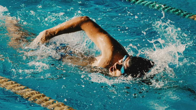 A swimmer moves through the water doing freestyle while wearing goggles during a lesson