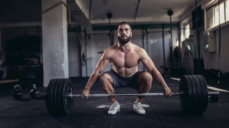 A man prepares to lift a loaded barbell, showing effort that often leads to teeth grinding among heavy lifters