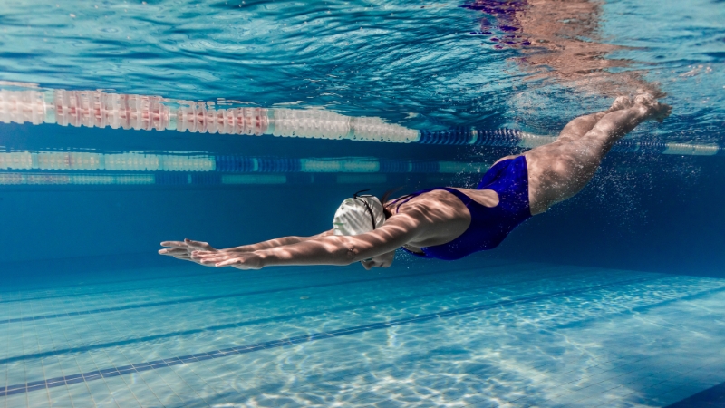 A swimmer glides underwater in a streamlined position, engaging core muscles to maintain balance and stability