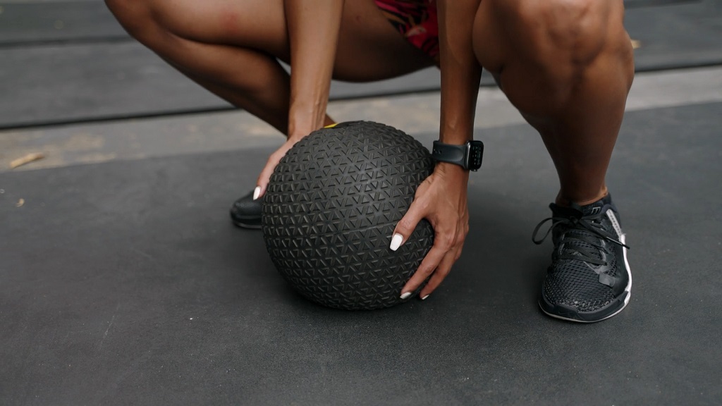 Close-up of a woman squatting and gripping a textured medicine ball before a workout, ideal for medicine ball ab workout