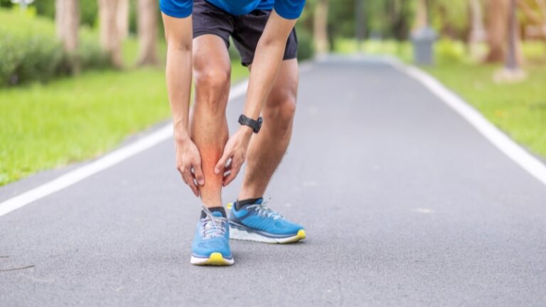 A runner stops on a paved path to hold his lower leg, showing clear shin splints pain during exercise