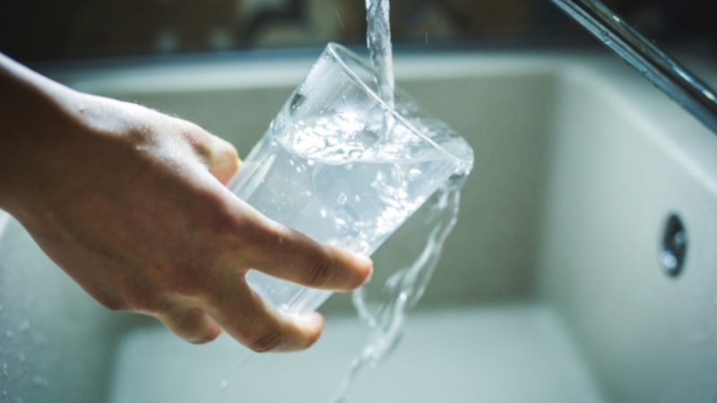 A person filling a glass of water at the sink as part of an evening hydration routine