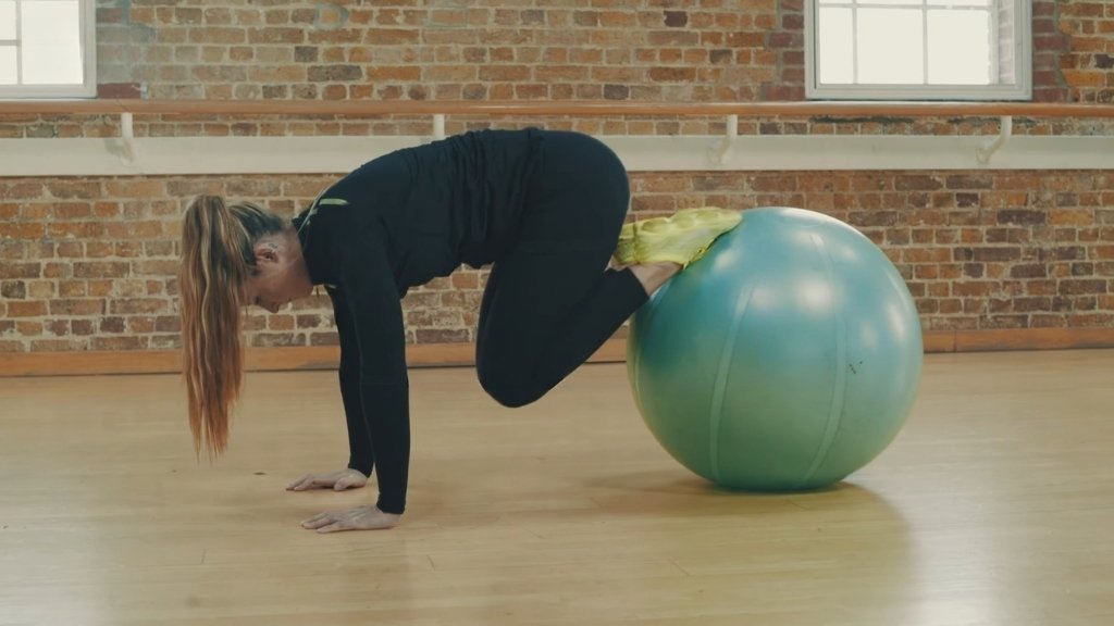 Knee tuck exercise on a stability ball to target core muscles