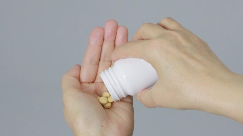 A person pouring magnesium tablets from a white bottle into their hand