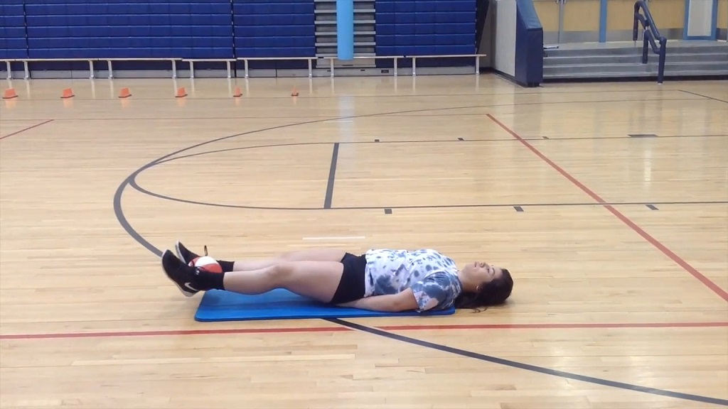 Athlete performing leg raises while holding a medicine ball between feet in a gym setting