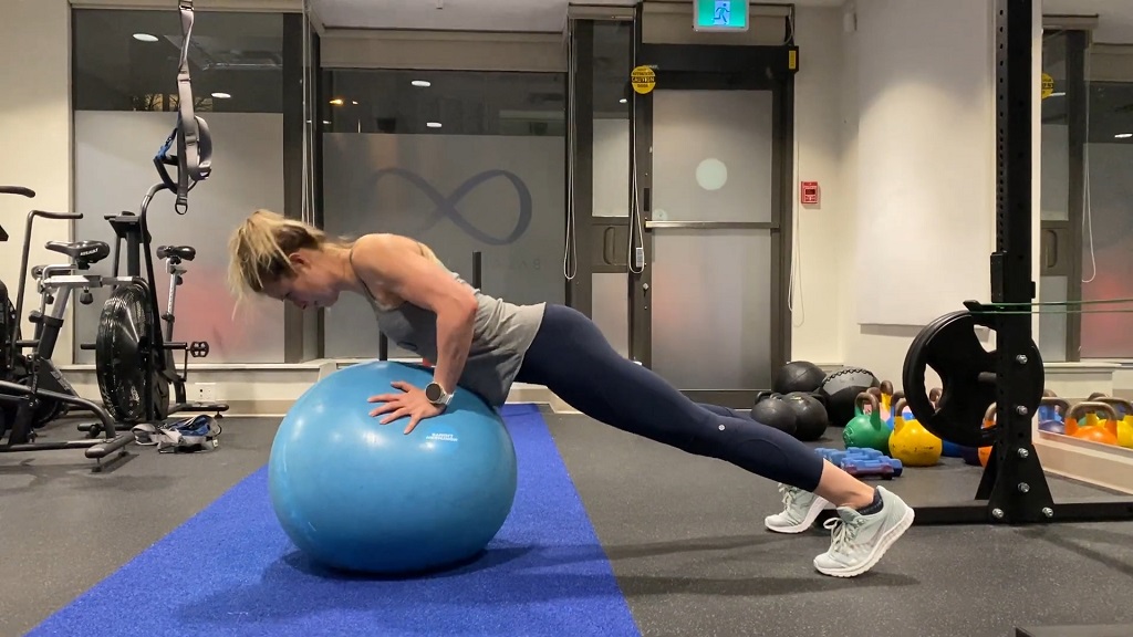 Woman performing pike push-up using a stability ball at the gym