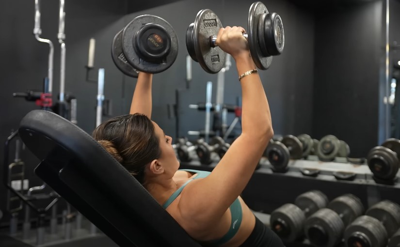A woman is lifting weights in a gym, focusing on her workout with determination and strength