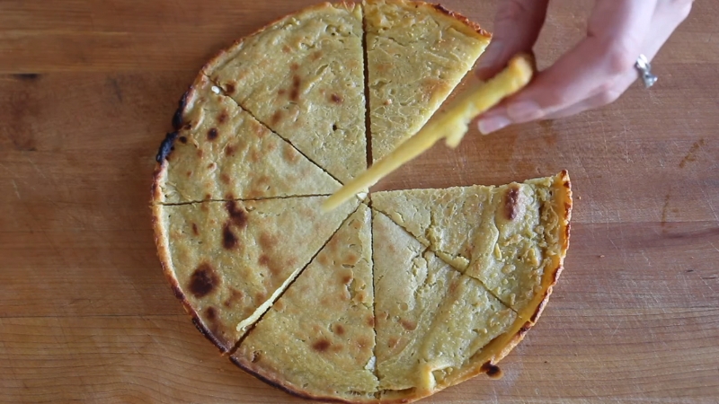 Sliced chickpea pancake served on a wooden surface, with one piece being lifted by hand
