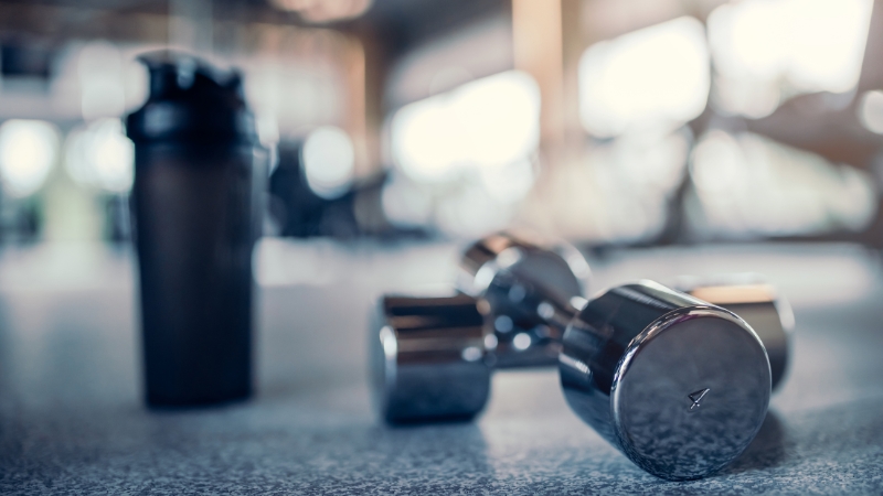 Two chrome dumbbells and a shaker bottle in a gym