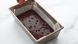 A parchment-lined baking pan filled with chocolate brownie batter topped with chocolate chips, ready to go in the oven