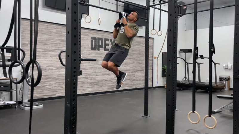 A man performs a towel pull-up in a gym, using grip-focused training to strengthen his forearms