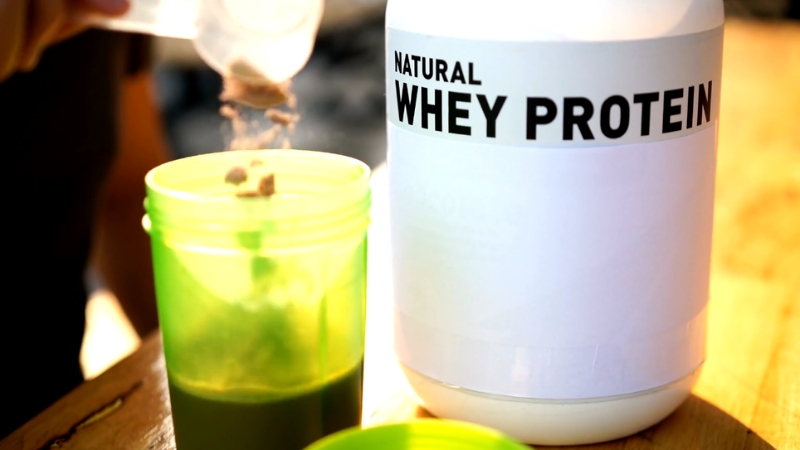 A scoop of natural whey protein powder being added to a shaker bottle after a workout