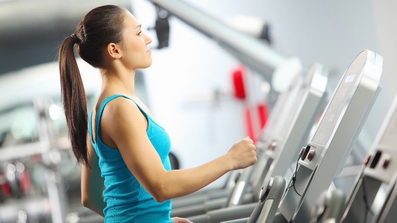 Woman on a treadmill wearing a fitted tank top, dressed for optimal comfort during cardio workouts at the gym