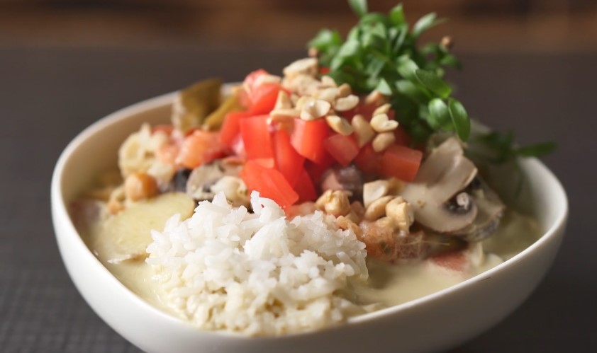 A bowl of Thai green curry served with a side of steamed rice, garnished with fresh herbs and colorful vegetables