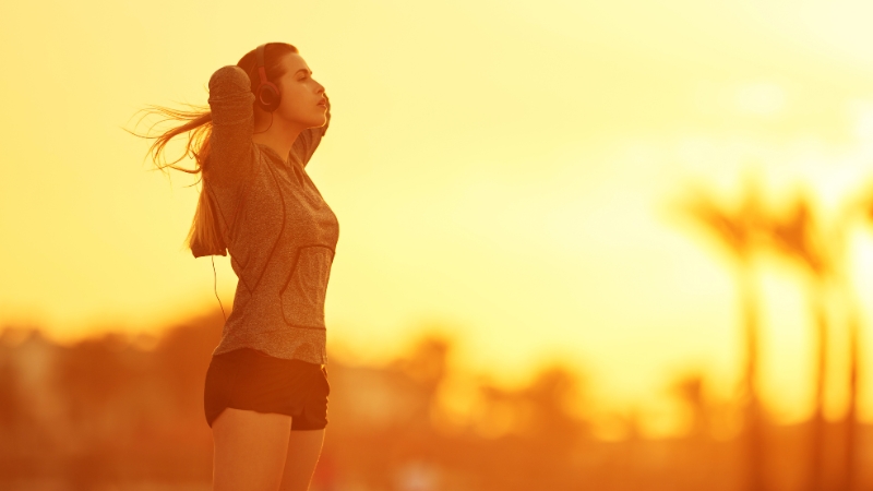 Woman stretching outdoors at sunset with headphones on before a workout during vacation