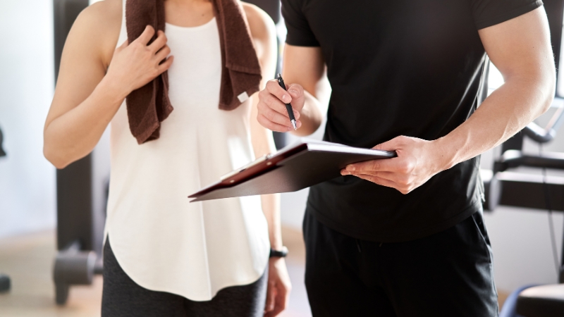 A personal trainer discussing a workout plan with a gym member holding a towel