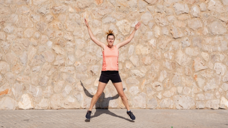 Woman doing jumping jacks outdoors in sportswear as part of a holiday HIIT workout