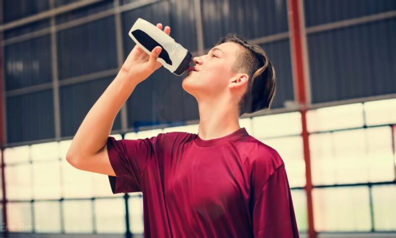 Athlete in a red shirt drinking from a sports bottle during a workout.